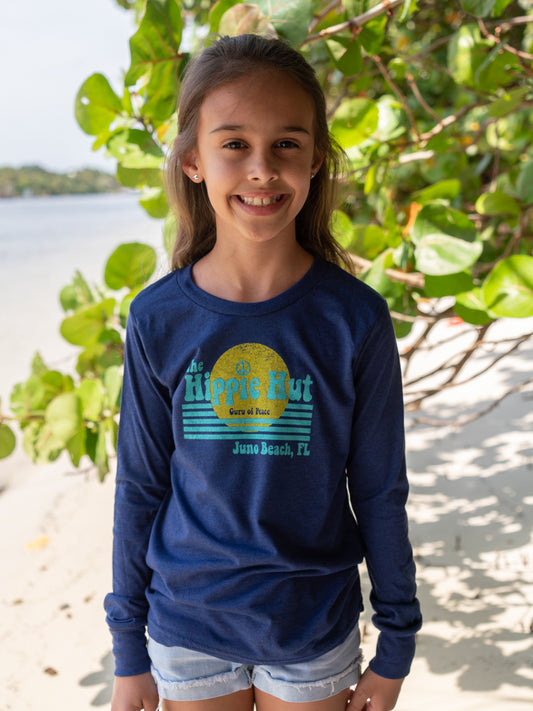 Young girl wearing a blue long-sleeve shirt with a graphic design, standing on a beach.