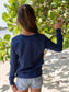Young girl wearing a blue long-sleeve shirt, standing on a beach.