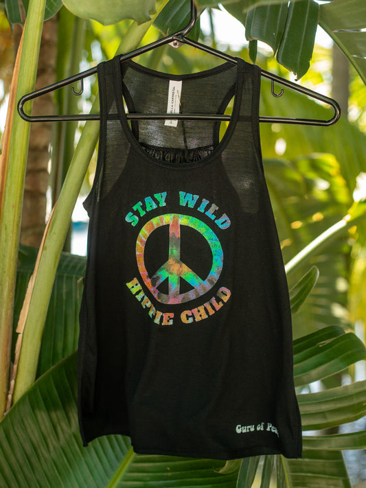Black tank top with colorful peace sign and text 'Stay Wild, Explore Child' on a hanger against a leafy green background.