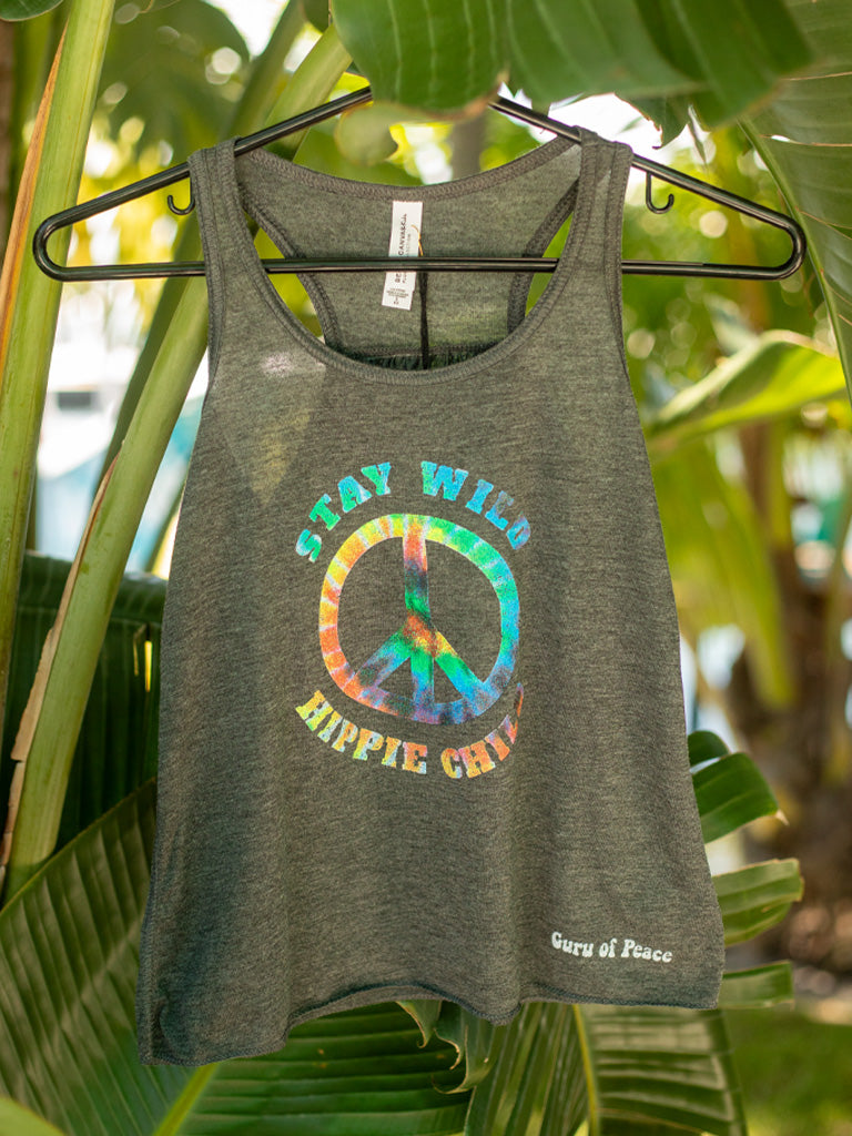 Grey tank top with colorful peace sign and text 'Stay Wild, Explore Child' on a hanger against a leafy green background.