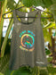 Grey tank top with colorful peace sign and text 'Stay Wild, Explore Child' on a hanger against a leafy green background.