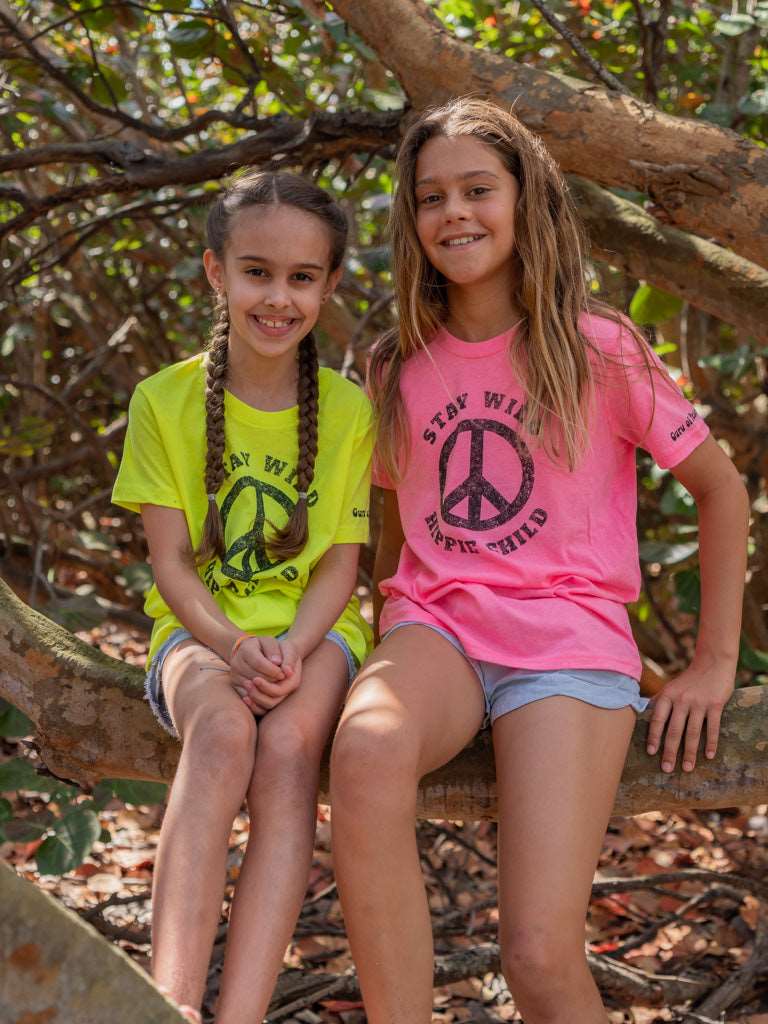 Two young girls sitting on a tree branch with peace signs on their shirts.