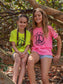 Two young girls sitting on a tree branch with peace signs on their shirts.
