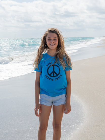 Young girl standing on a beach with a peace sign on her blue t-shirt.