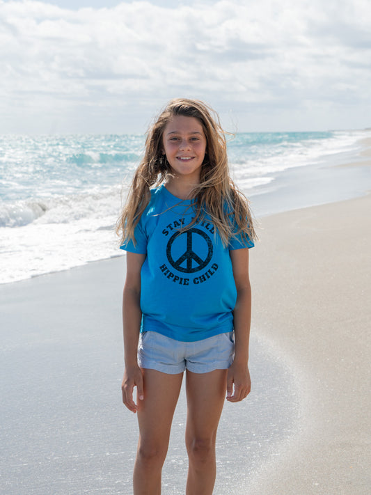 Young girl standing on a beach with a peace sign on her blue t-shirt.