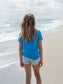 Young girl standing on a beach wearing a blue t-shirt.