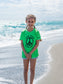 Young girl standing on a beach with a peace sign on her green shirt.