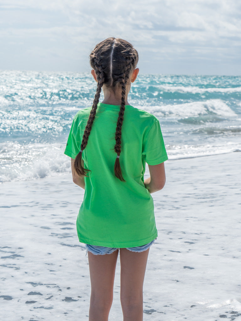 Young girl standing on a beach wearing a green t-shirt.