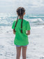 Young girl standing on a beach wearing a green t-shirt.