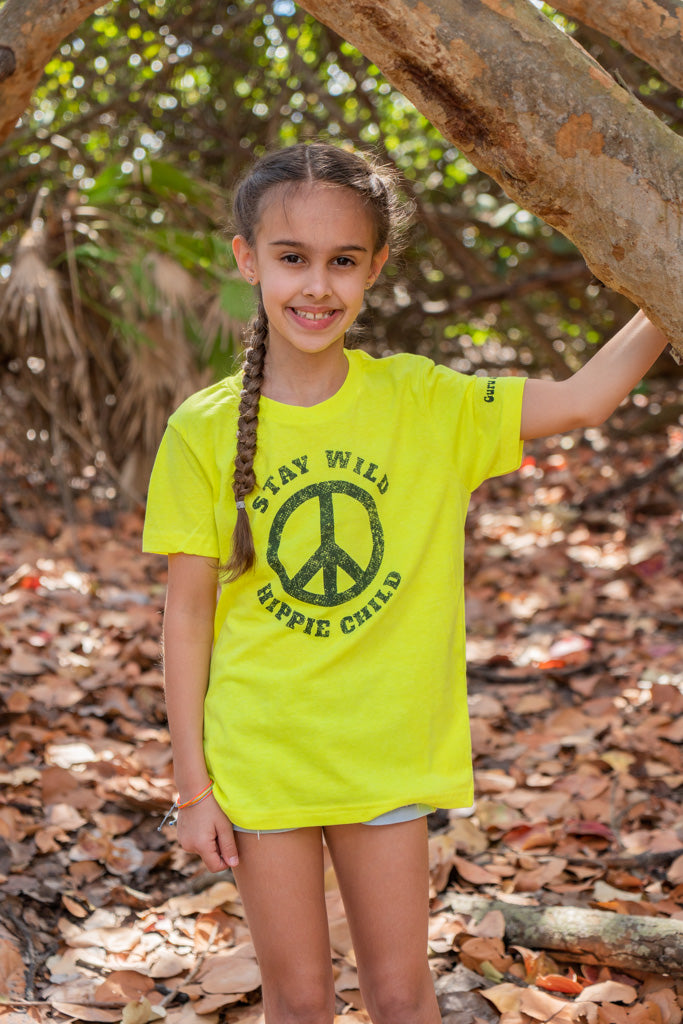 Young girl standing by a tree branch with a peace signs her yellow t-shirt.