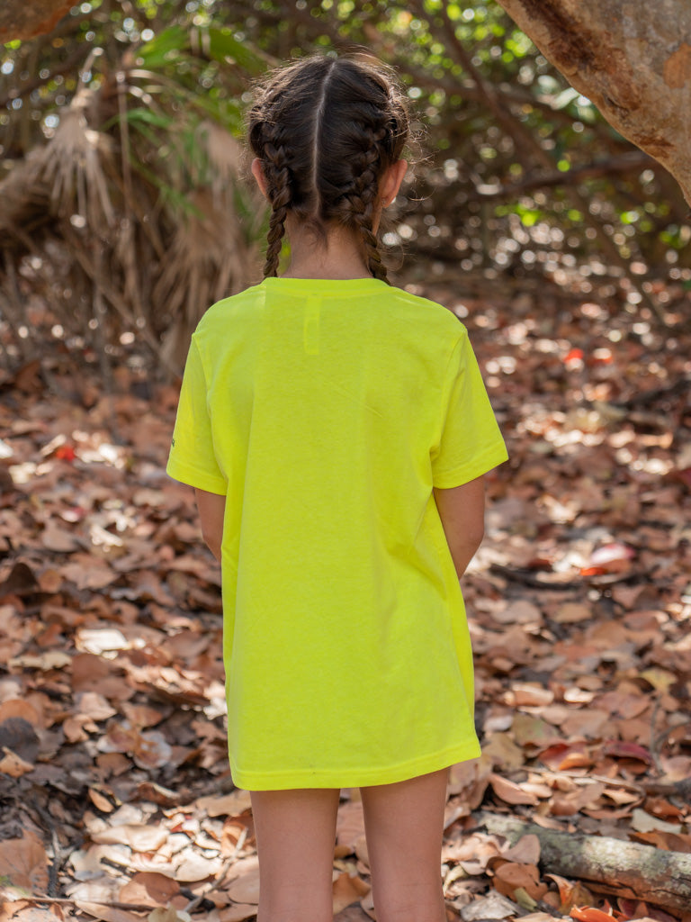 Young girl standing by a tree branch wearing a yellow t-shirt.
