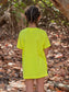 Young girl standing by a tree branch wearing a yellow t-shirt.