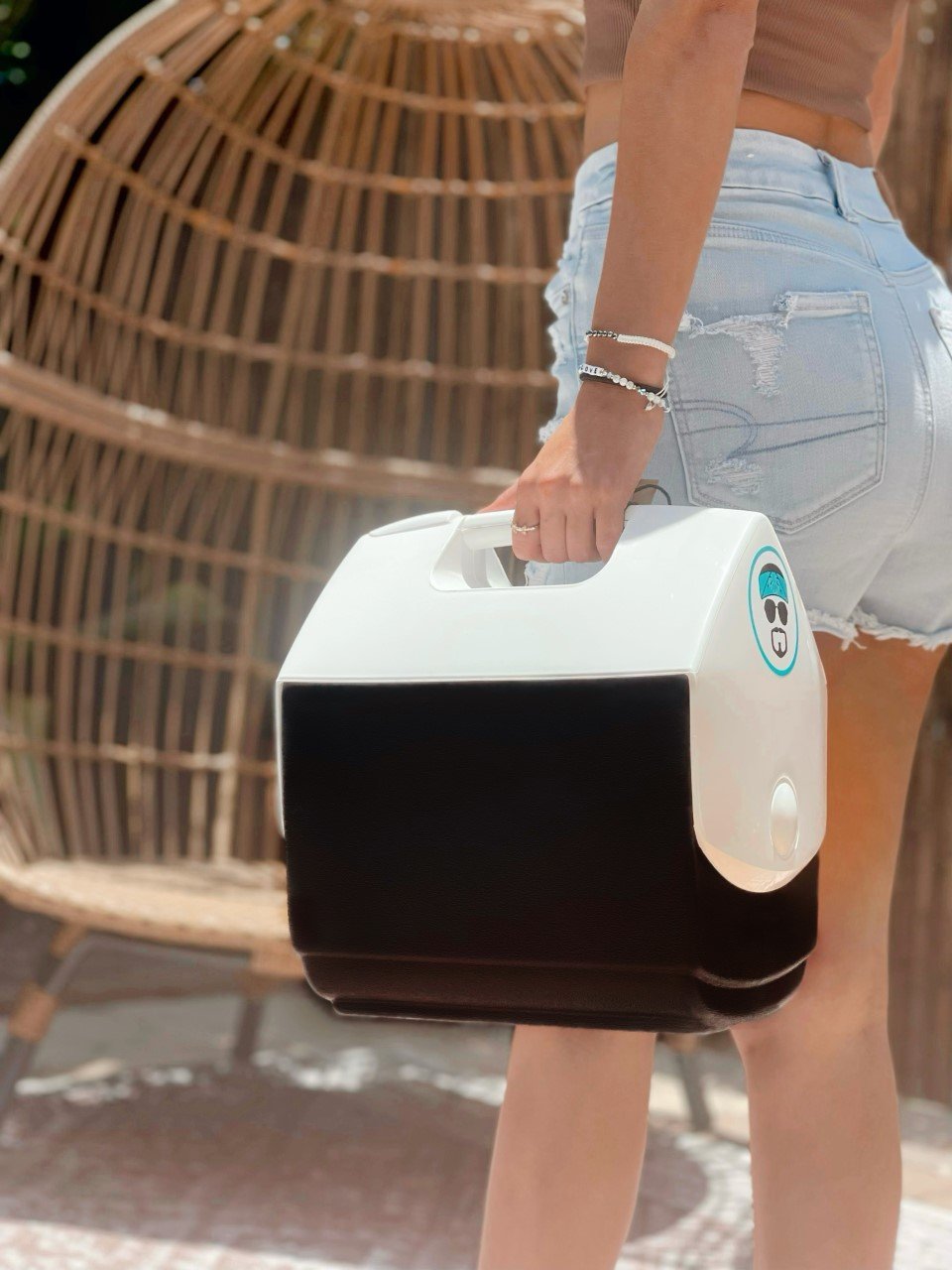 A person holding a white and black portable cooler with a tent-top design.